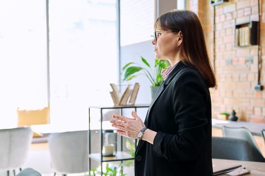 Thoughtful serious business mature woman looking out the window. Elegant middle-aged female manager director in suit, profile view. Business, success, reputation, perseverance, honesty concept