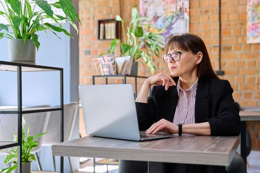 Middle-aged business confident successful serious woman working remotely at table with laptop computer in coworking cafe. Business, mature people, success, leadership, management, empowerment concept