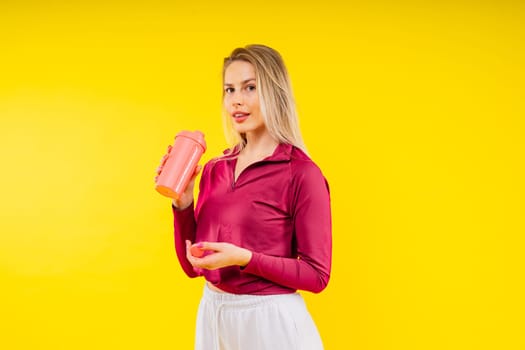 Happy beautiful brunette woman with water bottle or proteine shake on a yellow background