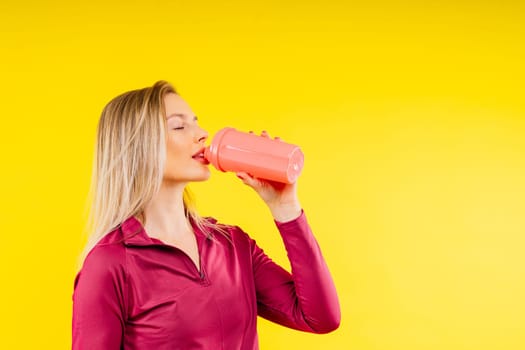 Happy beautiful brunette woman with water bottle or proteine shake on a yellow background