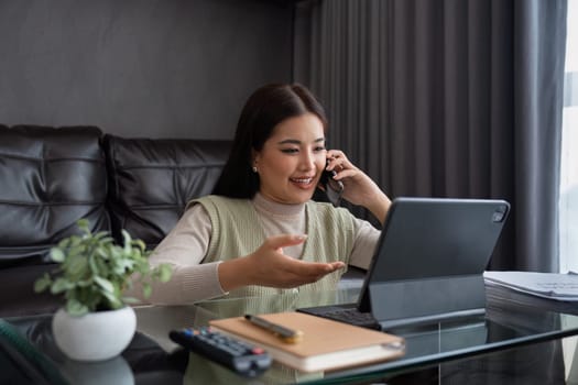 Asian business woman talking on mobile and working on laptop remotely from home. work from home concept.