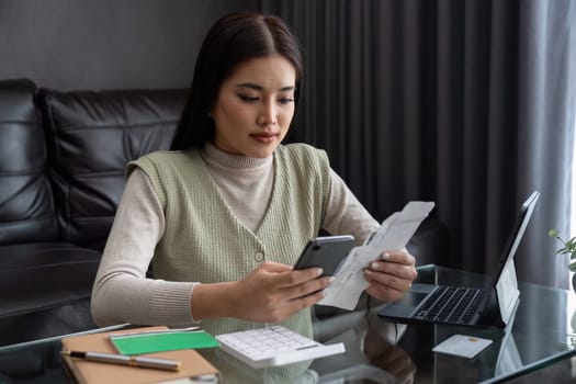 young woman calculate finance, hand holding mobile phone and invoice paper, pay from bills tax.