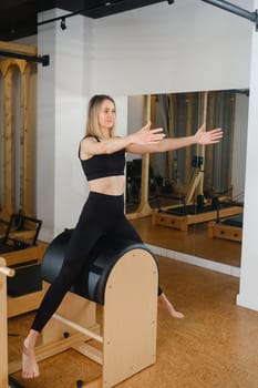 Young girl doing Pilates barre in a gym. Beautiful slim woman in black clothes performs exercises to strengthen the spine and back muscles.