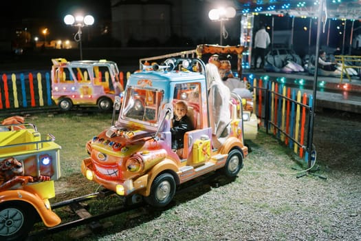 Little girl sits in a children train carriage at a fair. High quality photo