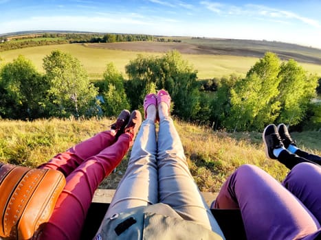 Legs of people on a swing over a beautiful natural landscape in summer or spring. Friends Enjoying Scenic Overlook at Sunset the view from hilltop