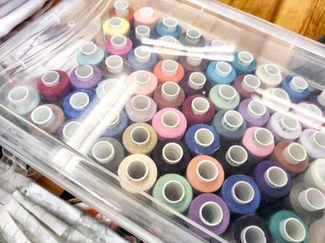 Vibrant Array of Thread Spools in Transparent Storage Box. Colorful thread spools neatly arranged in a clear plastic container