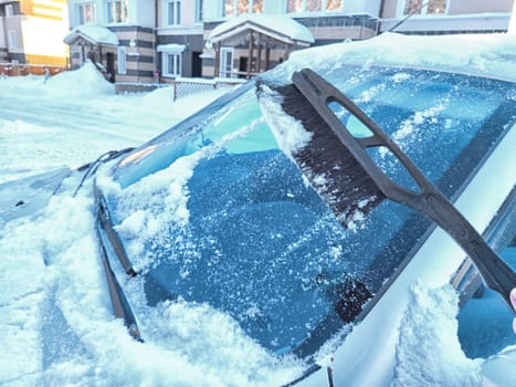 Winter Morning Car Snow Clearing. Person brushing snow off car on frosty winter morning. Difficulties in travel and trip in cold months