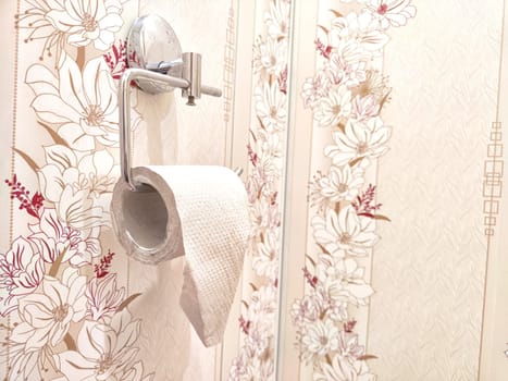 Toilet paper on chrome holder against decorative floral wallpaper. Restroom Toilet Paper Holder With Floral Wallpaper