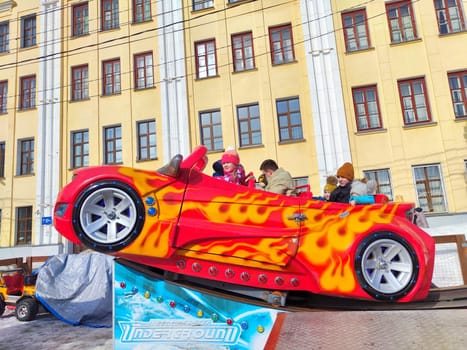 Kirov, Russia - March 17, 2024: People enjoy ride in whimsically designed flame-decorated carousel car. Amusement Ride Fun With Flaming Red Car
