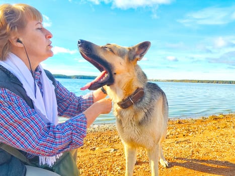 Adult girl with shepherd dog taking selfie near water of lake or river. Middle aged woman and big pet on nature. Friendship, love, fun, hugs