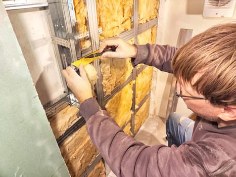 Professional Installs Drywall During Home Renovation. A skilled worker measures and secures drywall in a home under renovation