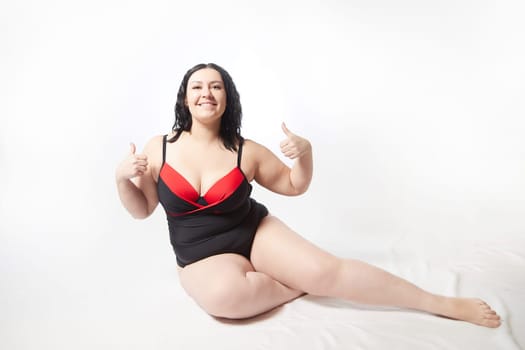 Portrait of attractive dreamy thick woman in red black swimsuit posing on white background. Body positive, photoshoot, selfie. Funny plus size model