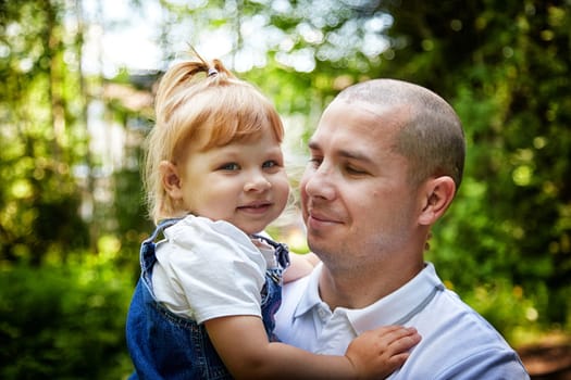 Gentle Father Holding Young Daughter Outdoors in Daylight. A tender moment as dad embraces his little girl in a sunny garden