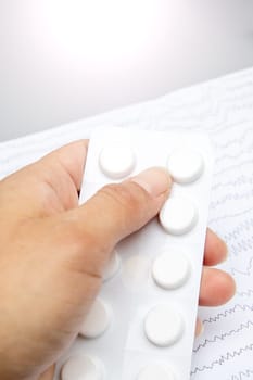 The person is delicately holding a blister pack of pills between their thumb and index finger. The packaging contrasts with their trendy fashion accessory