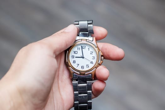 The person is wearing an analog watch on their wrist, displaying the time. The font on the watch is clearly visible, held in their hand with a relaxed gesture