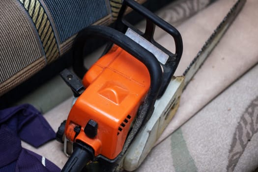 A chainsaw is resting on a hardwood flooring. The machine is powered by gas and is commonly used in automotive tire and wheel systems. It has metal parts