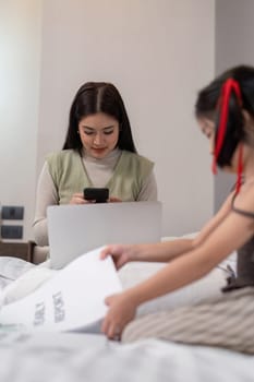 Mom work from home with children. Mother working on bed laptop in bedroom with child daughter. Funny authentic lifestyle family moment.