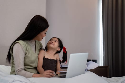 Mom work from home with children. Mother working on bed laptop in bedroom with child daughter. Funny authentic lifestyle family moment.