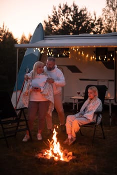 The family is relaxing together by the campfire near their mobile home. Evening family vacation.