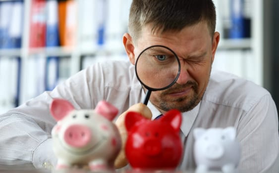 Male businessman examining group of piggybanks trying to find money portrait