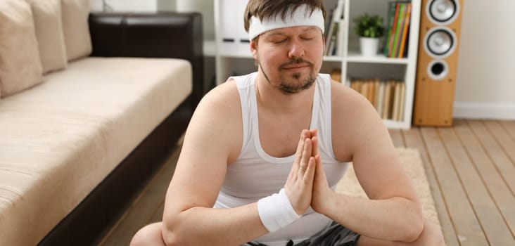 A young man practicing yoga and Pilates at home dreams of an excellent figure being restored after an intense load for the body to lose weight.