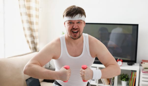 Young attractive man engaged in fitness at home holding dumbbell in hand trying to fight excess weight and loss