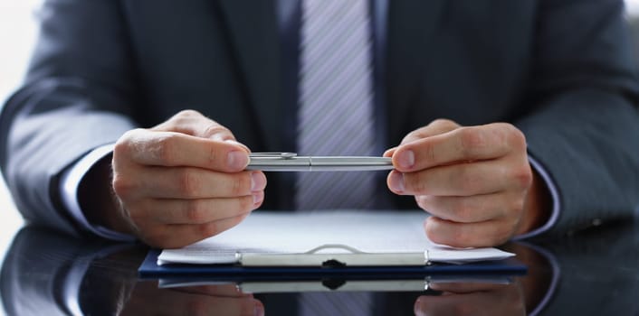 Male arm in suit and tie fill form clipped to pad with silver pen closeup. Sign gesture read pact sale agent bank job make note loan credit mortgage investment finance chief legal law concept