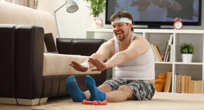 Young attractive fitness man lies on a fat mat with overweight performs stretching exercises and smiles