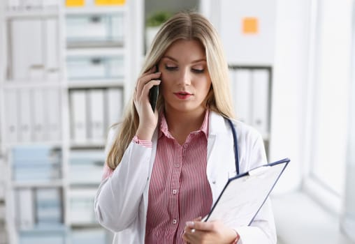 Beautiful female blond doctor talking on phone at the office woman discussing the disease and giving online consultation remote training education