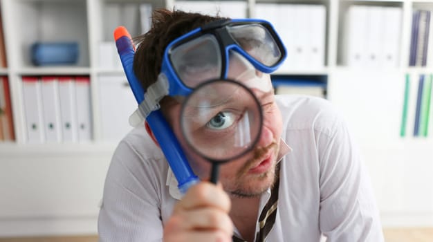Funny smiling man wearing suit and tie in goggles and snorkel hold in arm magnifier glass at workplace in office portrait closeup. Searching data at online web about tourism 404 page error