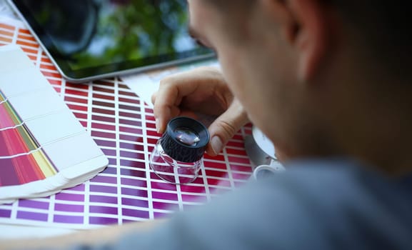 Male serviceman hold in hand magnifying glass making colour test at worktable for further promotion closeup