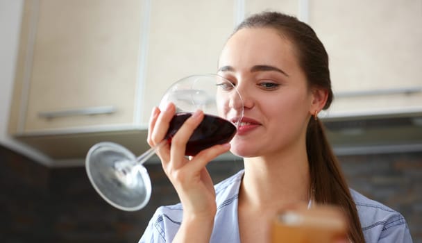 Beautiful smiling brunette woman hold in arms glass of red wine at kitchen table portrait. Vine cabernet merlot sauvignon lips beauty concept