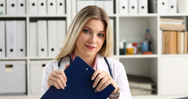 Beautiful smiling female doctor hold clipboard pad and fill something with silver pen. Physical illness prevention prescribe remedy ward round therapeutist assistance healthy lifestyle concept