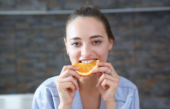 Beautiful brunette smiling woman eat sliced raw tasty orange half at kitchen in the morning portrait. Weight loss beauty fit concept