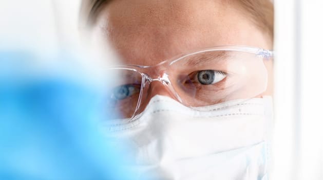 A portrait of a young surgeon chemist's doctor looks at a container with a blue liquid and a mask is fought with viruses and a vaccine for vaccines against diseases.
