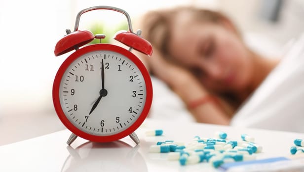 Pieces are scattered on the table near alarm clock which shows 7 am. Young woman sleeping in bed on the effects of narcotic pharmaceutical medications