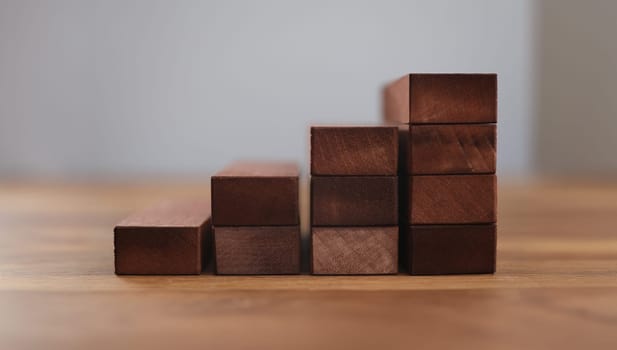 Close-up of wooden cubes arrange in pyramid shape. Brown blocks stacking as step stair. Ladder career path and business growth concept. Blurred grey background