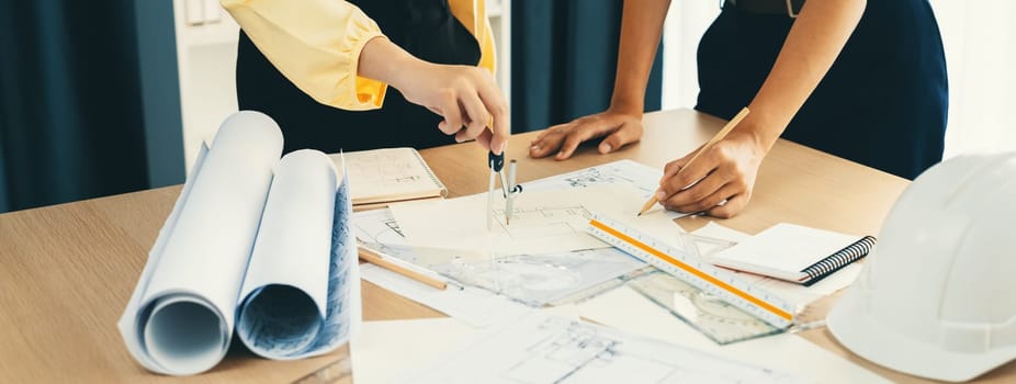 Professional architect team used divider measure during draft blueprint on table with architectural document, safety helmet and blueprint scatter around. Closeup. Focus on hand. Delineation.