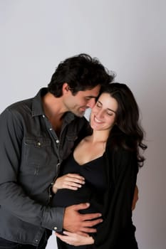Expectant couple sharing a loving moment, with hands on the pregnant belly, standing against a neutral background