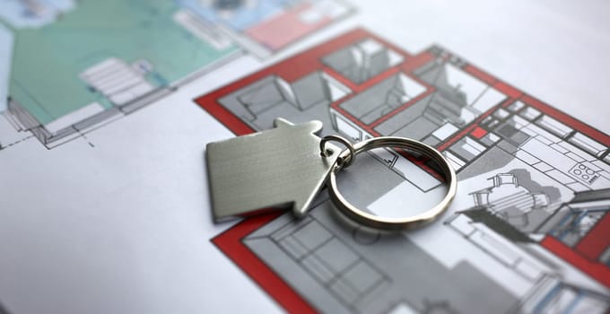 Metal key chain in form miniature house lies on paper project of apartment concept closeup