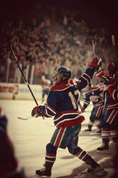 Hockey player in red celebrating a win with fists pumped in the air, illuminated by the spotlight