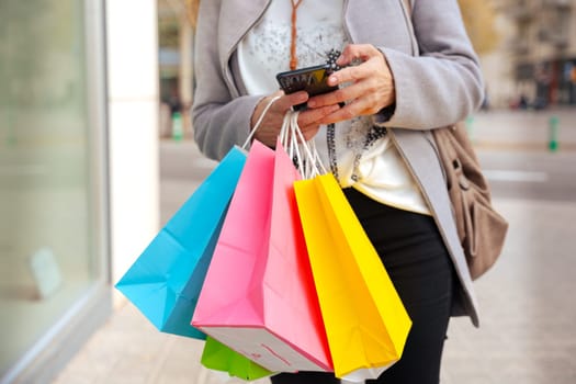 Woman shopping. Happy woman with shopping bags surfing internet with mobile phone online shopping. Consumerism, shopping, lifestyle concept