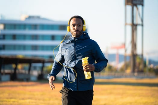 Young runner wearing headphones holding cold isotonic sports water in his hand outdoor.