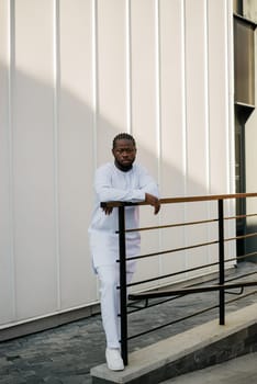 Cheerful male tourist dress in white wear dashiki ethnic smiling at city street on stairs. African American travel model have free time.