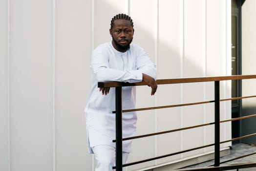 Cheerful male tourist dress in white wear dashiki ethnic smiling at city street on stairs. African American travel model have free time.