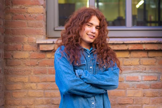 Attractive confident Caucasian teenage student with arms crossed looking at camera outdoors. Boy standing with happy face.