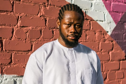 Close up portrait of a happy african american man smiling wearing ethnic dashiki clothes outdoor in summer street colourful brick wall. Millennial generation student and youth. Copy space.