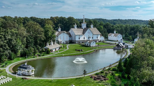 Elizabethtown, Pennsylvania, USA, August 11, 2023 - Aerial View Showcasing A Cluster Of Traditional White Orthodox Churches With Cross-Topped Domes, Arranged Around A Curved Pond With A Fountain, Amidst Green Trees And Neatly Arranged White Benches