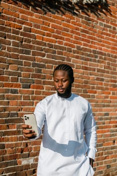 Happy young African American man in dashiki ethnic clothes taking selfie on brick wall background. Millennial generation student and youth