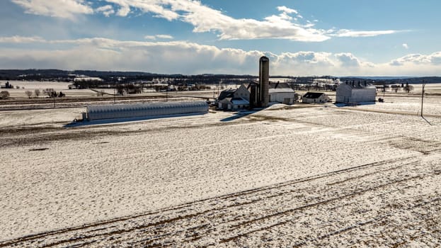 An Aerial View Of A Snow-Covered Farm With Multiple Buildings And Silos.